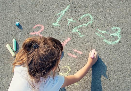 Fillette qui écrit des additions à la craie par terre